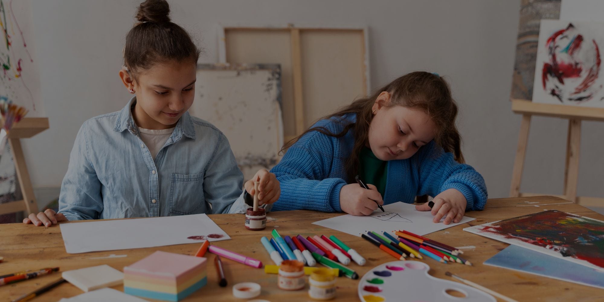 Two children sitting at a table with art supplies, engaged in an activity.