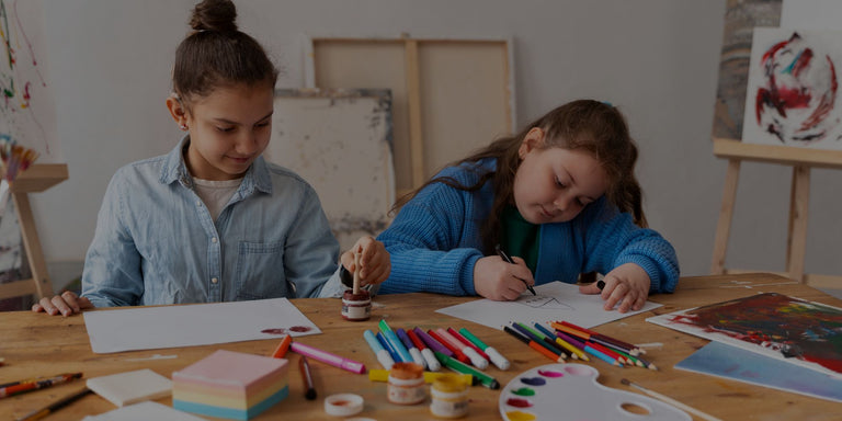 Two children sitting at a table with art supplies, engaged in an activity.
